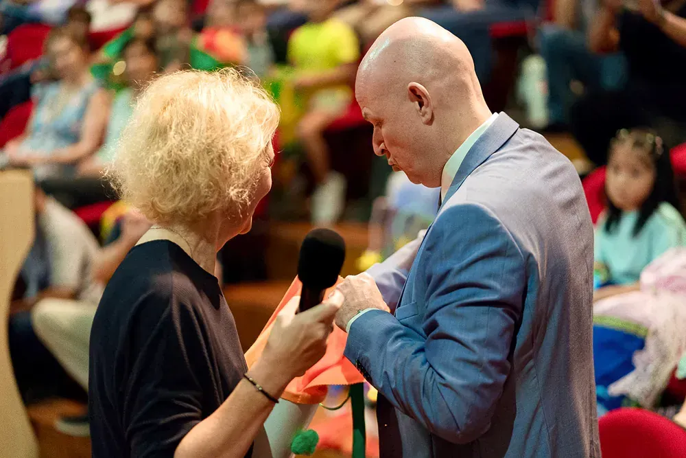 A man and a woman are talking into a microphone in front of a crowd.