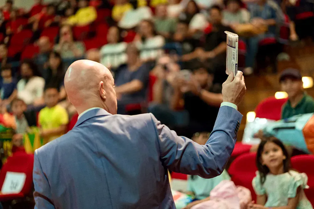 A man in a suit is holding a piece of paper in front of a crowd of people.