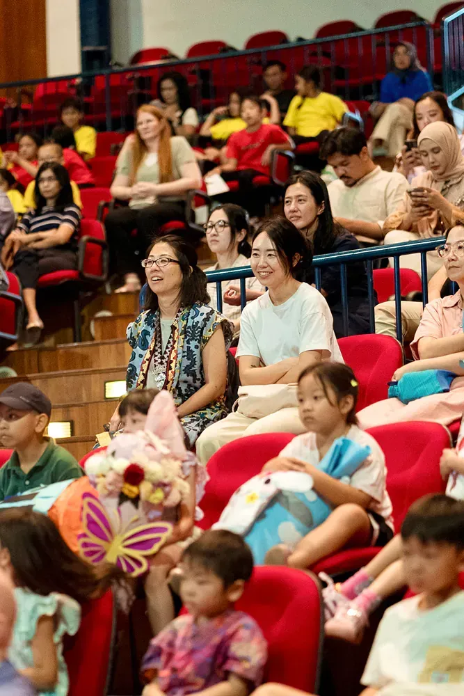 A large group of people are sitting in red chairs in an auditorium.