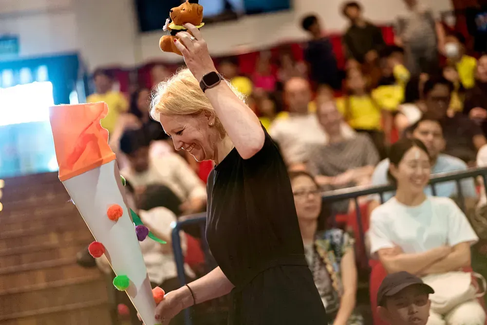 A woman is holding a stuffed animal in front of a crowd of people.