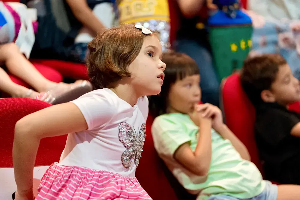 A group of children are sitting in red chairs in a theater.
