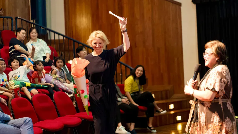 A woman is holding a wand in front of a crowd of people in an auditorium.