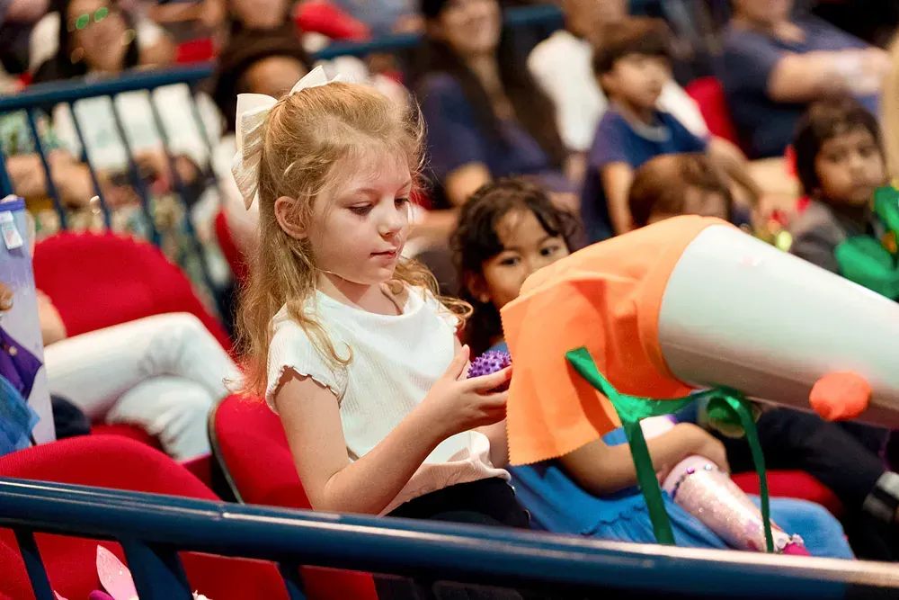 A little girl is sitting in a stadium with a megaphone in her hand.