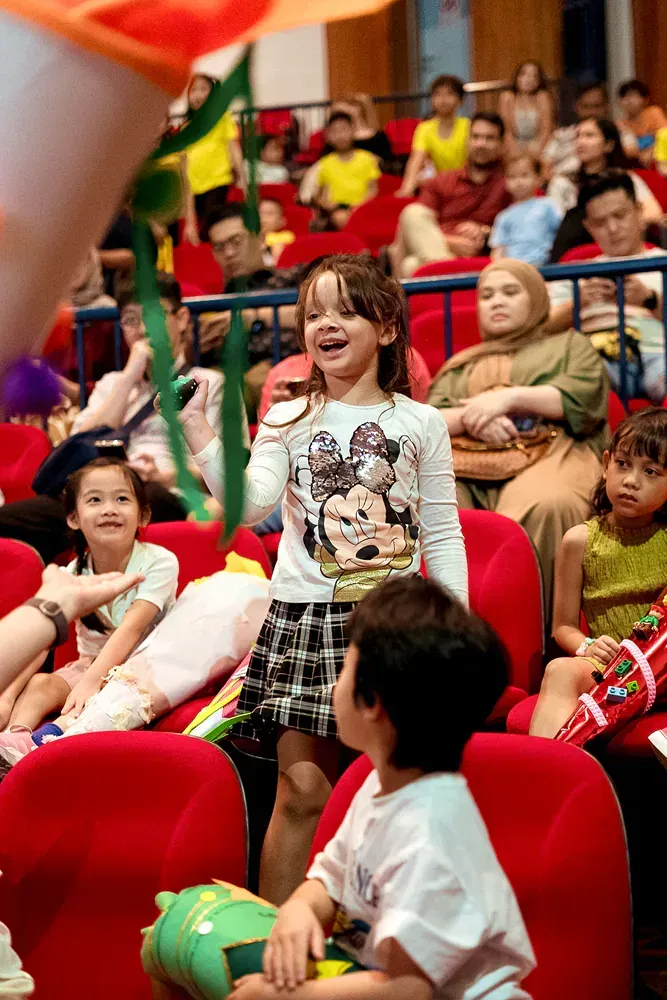 A group of children are sitting in red chairs in a theater.