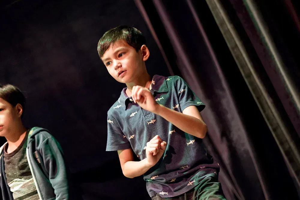 Two young boys are standing on a stage in front of a purple curtain.