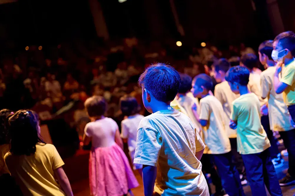 A group of children are standing on a stage in front of a crowd.