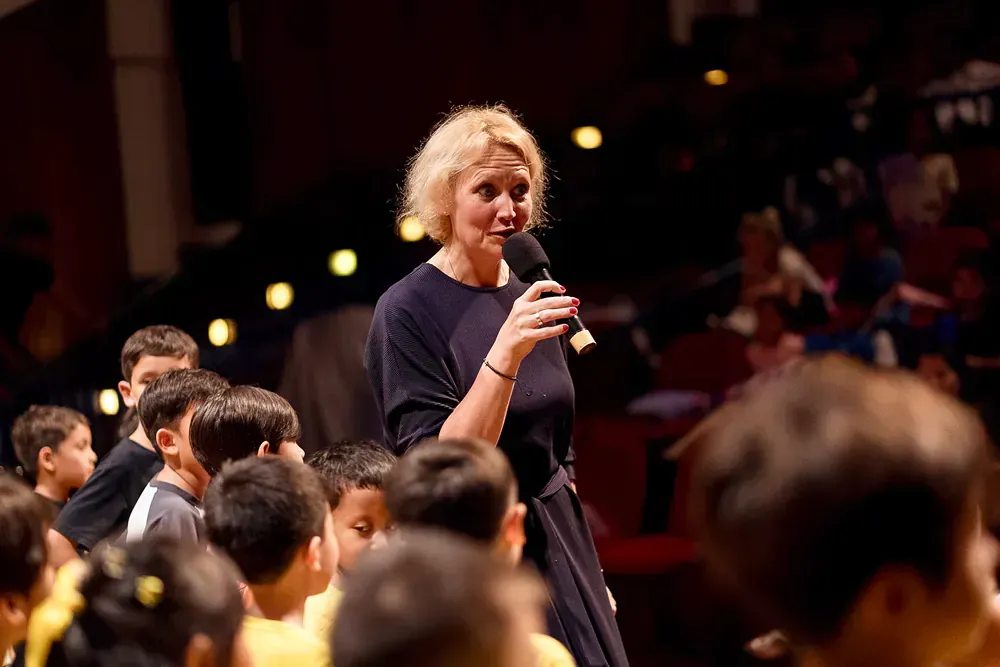 A woman is holding a microphone in front of a crowd of children.
