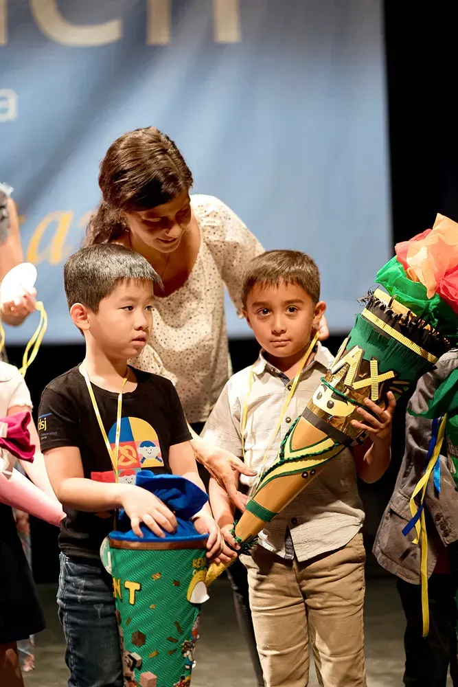 A woman is standing next to a group of children holding cones.