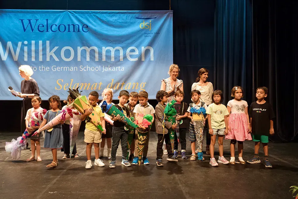 A group of children are standing on a stage in front of a welcome sign.