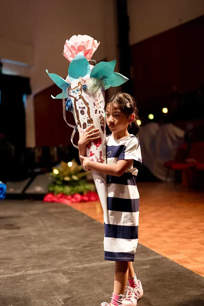 A little girl in a striped dress is holding a cone with flowers in it.