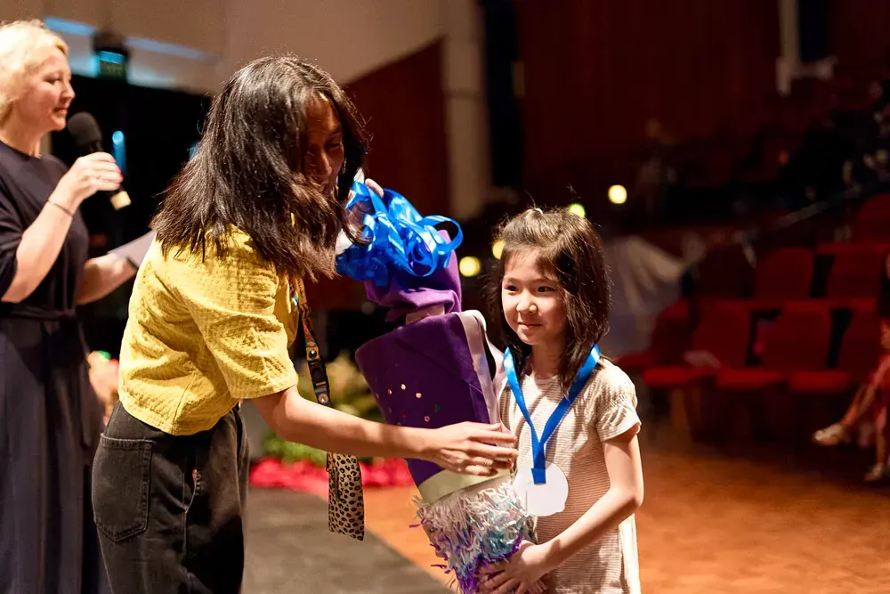 A woman is giving a girl a bouquet of flowers and a medal.