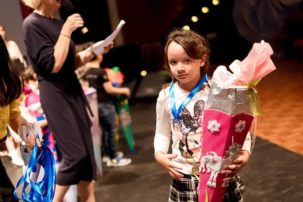 A little girl is holding a cone with a medal around her neck.