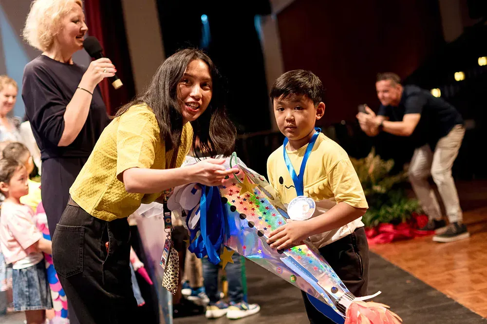 A woman is giving a medal to a young boy on a stage.