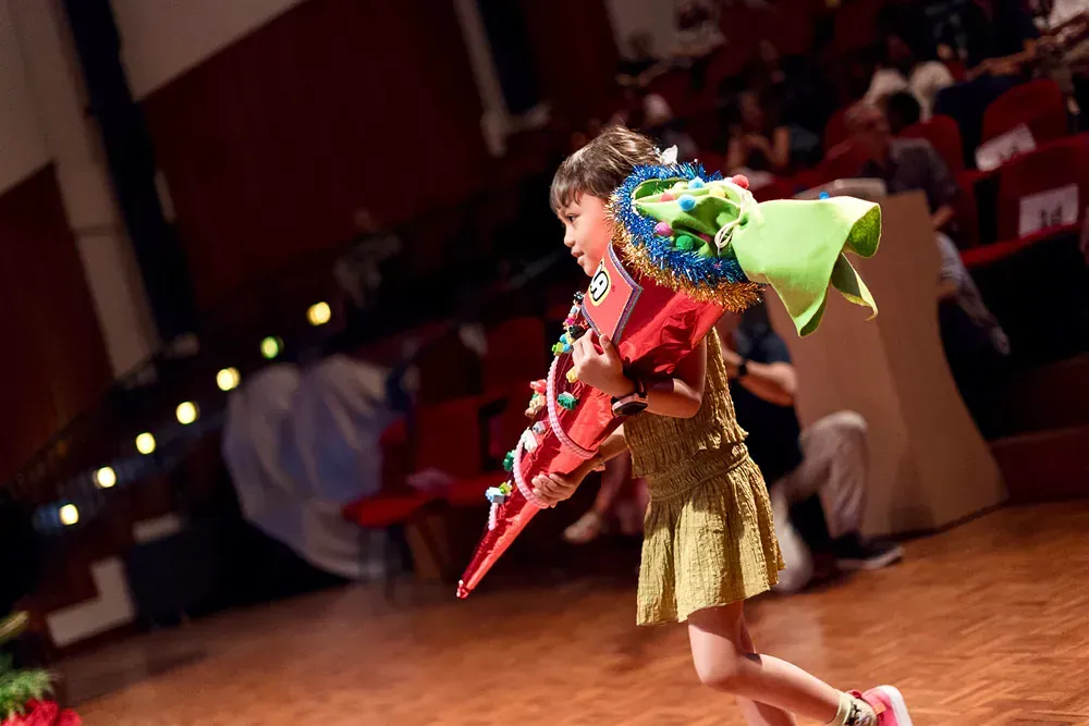 A little girl is holding a red guitar on a stage.
