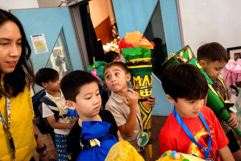 A group of children are standing in a room with a woman.