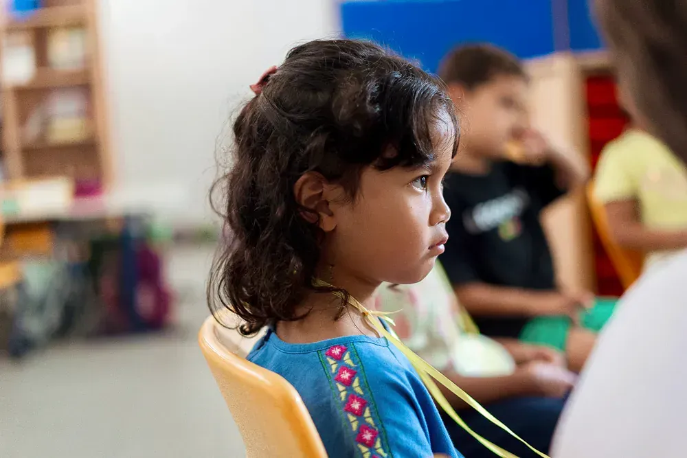 A little girl is sitting in a yellow chair in a classroom.