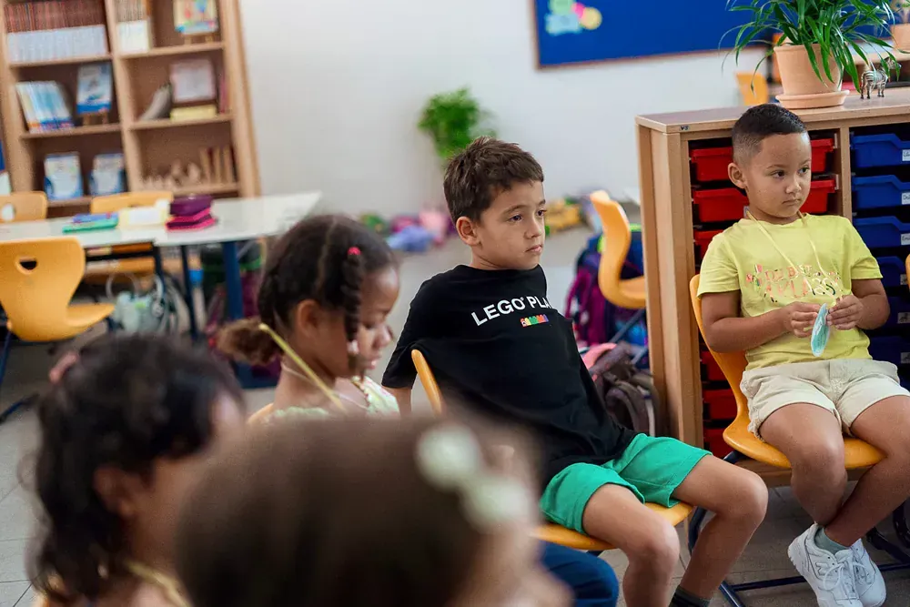 A group of children are sitting in chairs in a classroom.