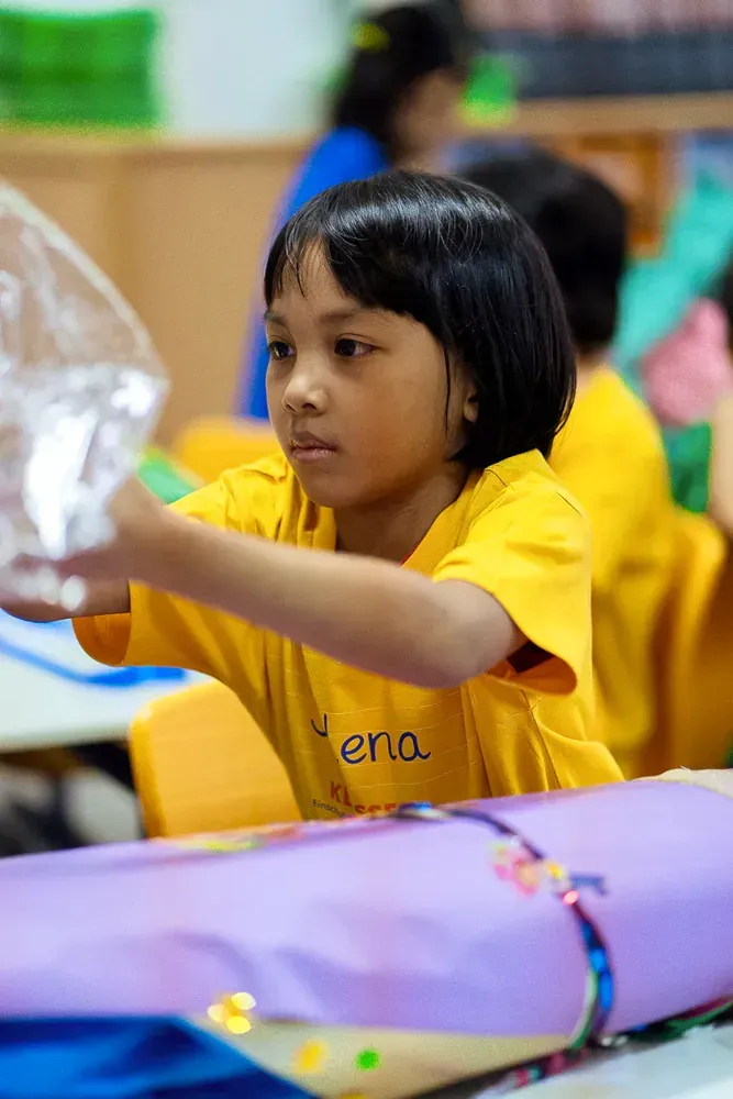 A young girl in a yellow shirt is holding a glass in her hand.