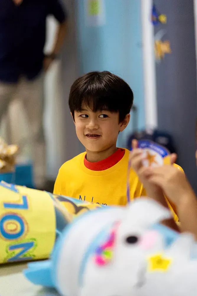 A young boy in a yellow shirt is sitting at a table with stuffed animals.