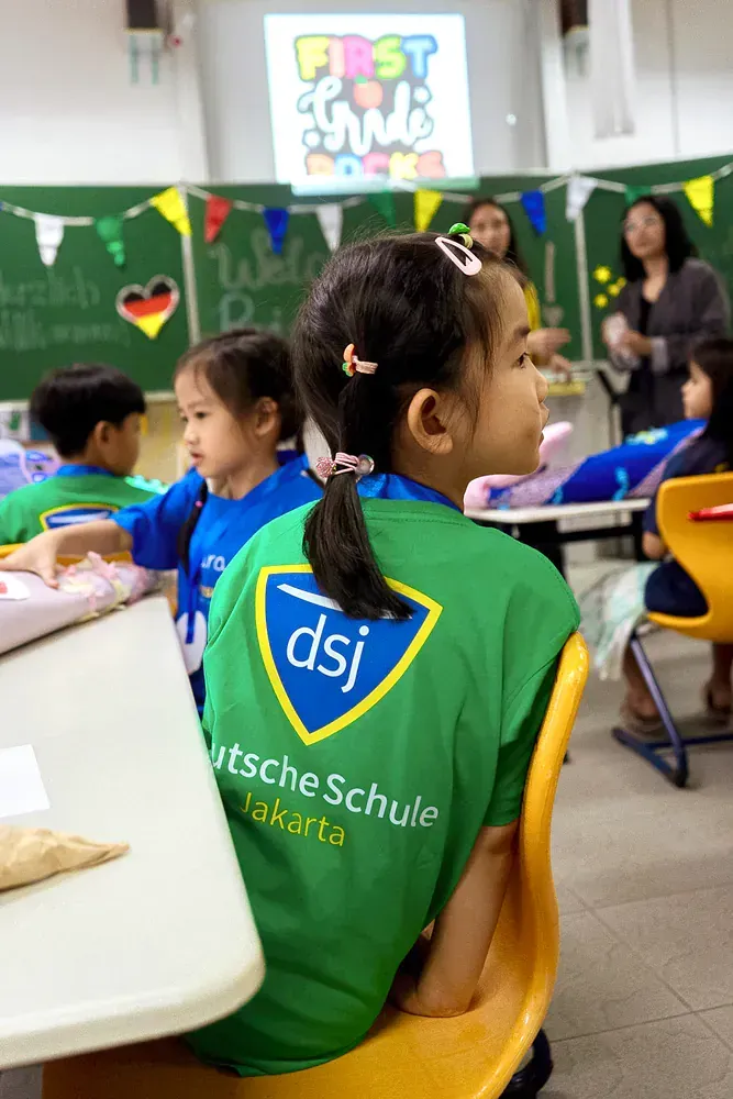 A girl wearing a green shirt that says dsj sits in a classroom