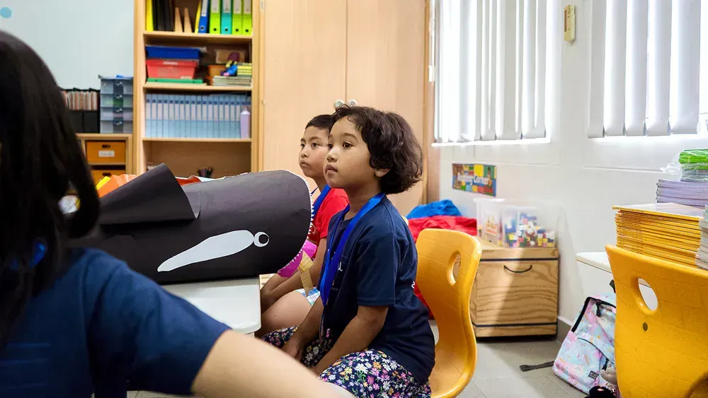 A group of children are sitting at a table in a classroom.