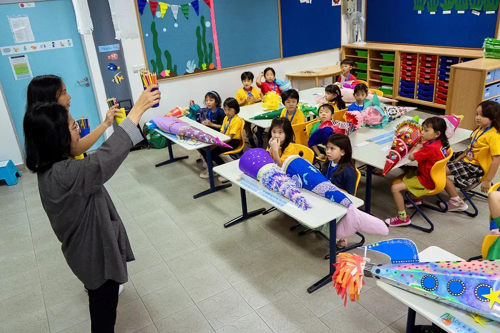 A woman is taking a picture of a group of children in a classroom.
