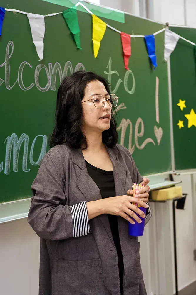 A woman is standing in front of a green chalkboard holding a cup.