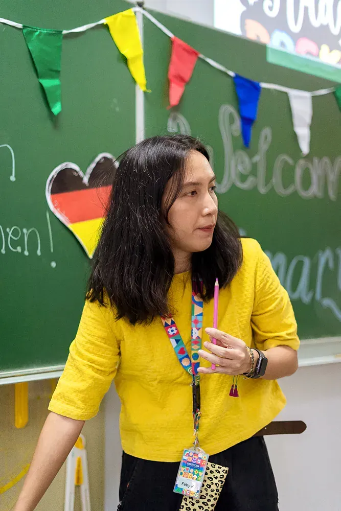 A woman in a yellow shirt is standing in front of a green board.