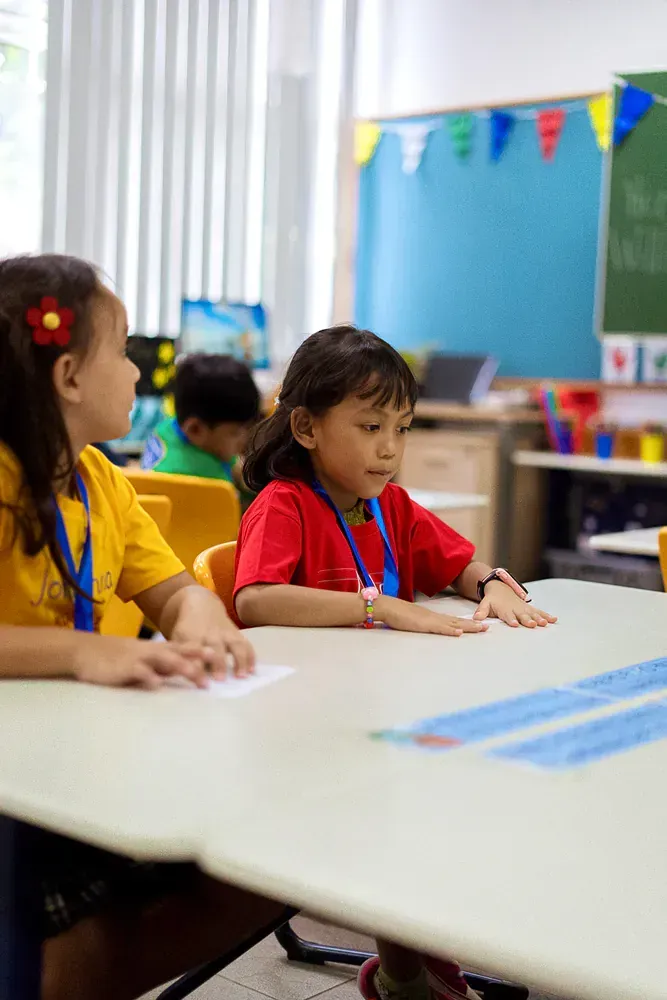 Two young girls are sitting at a table in a classroom.