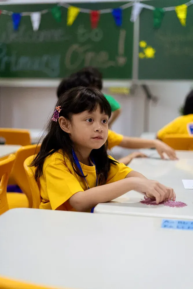 A little girl is sitting at a desk in a classroom.