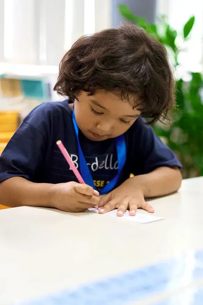 A young boy is sitting at a table writing on a piece of paper.