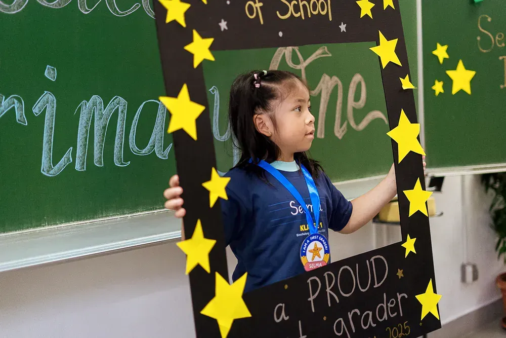 A little girl is holding a sign that says proud a grader