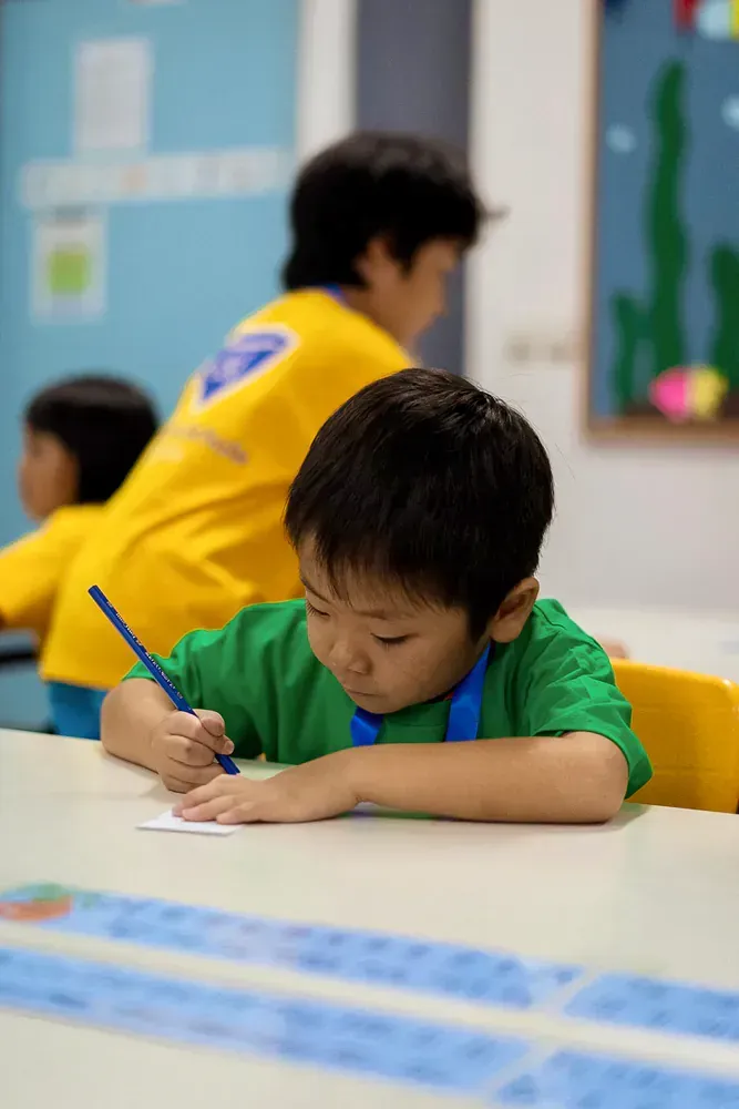 A young boy is sitting at a table writing on a piece of paper.