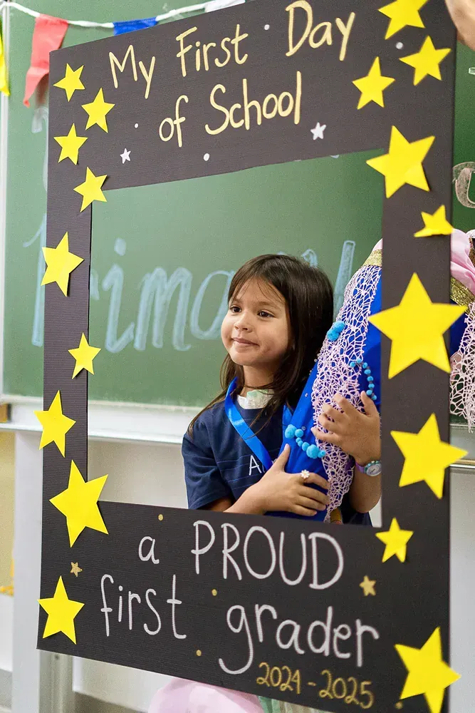 A little girl is standing in front of a sign that says my first day of school a proud first grader