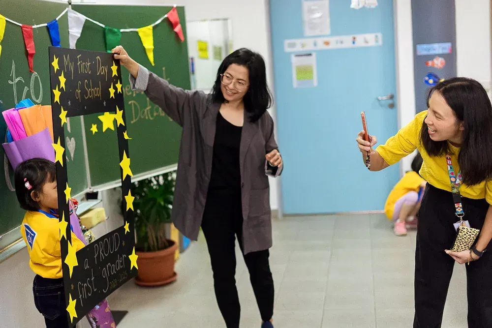 Two women are standing next to each other in front of a green board.