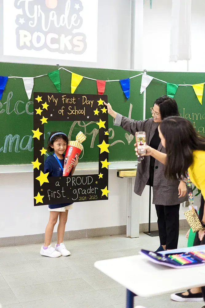 A girl is standing in front of a chalkboard in a classroom holding a picture frame.