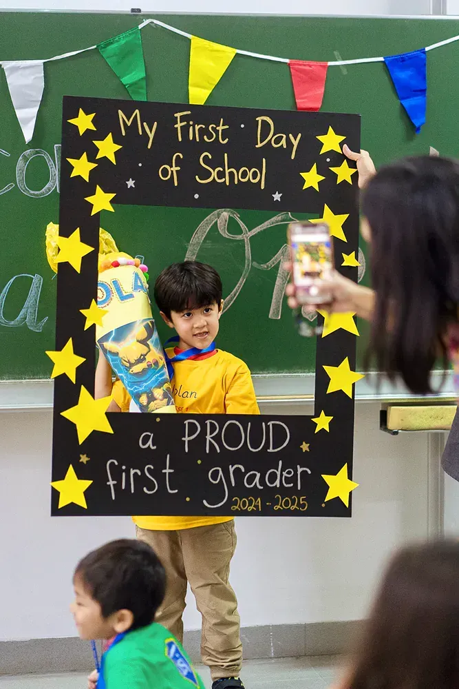 A boy is standing in front of a sign that says my first day of school