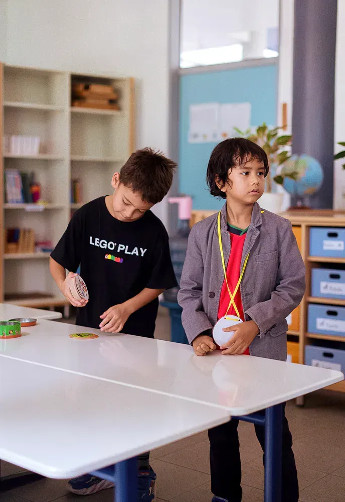 Two young boys are playing ping pong in a classroom.