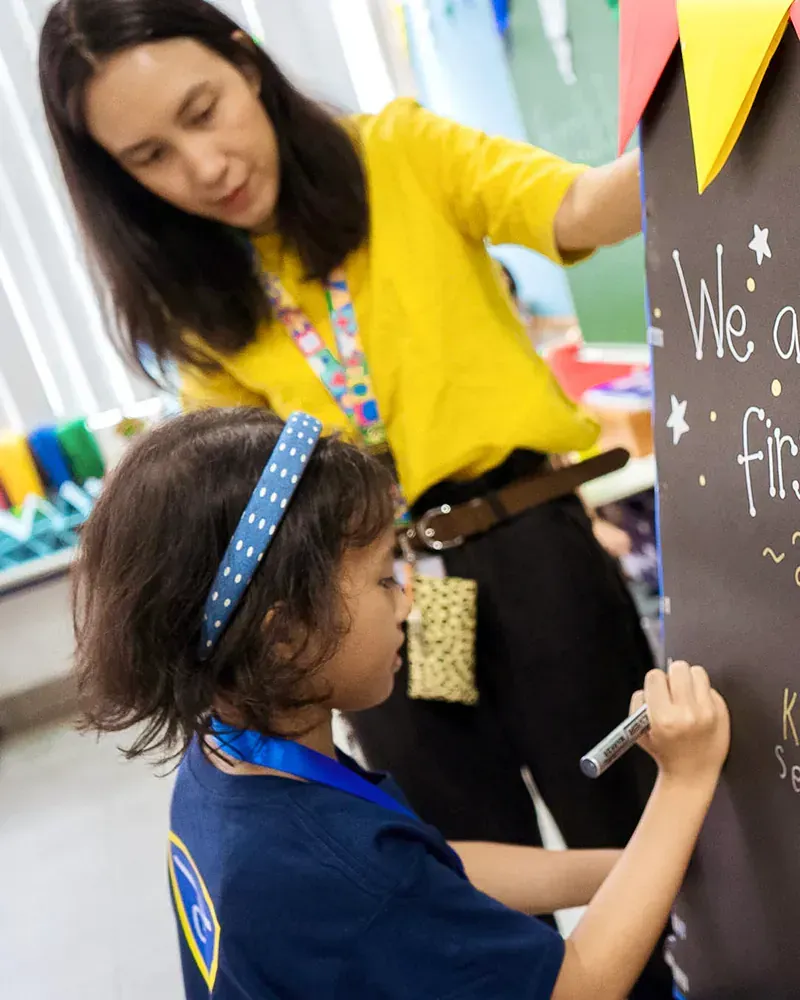 A little girl is writing on a blackboard that says we are first