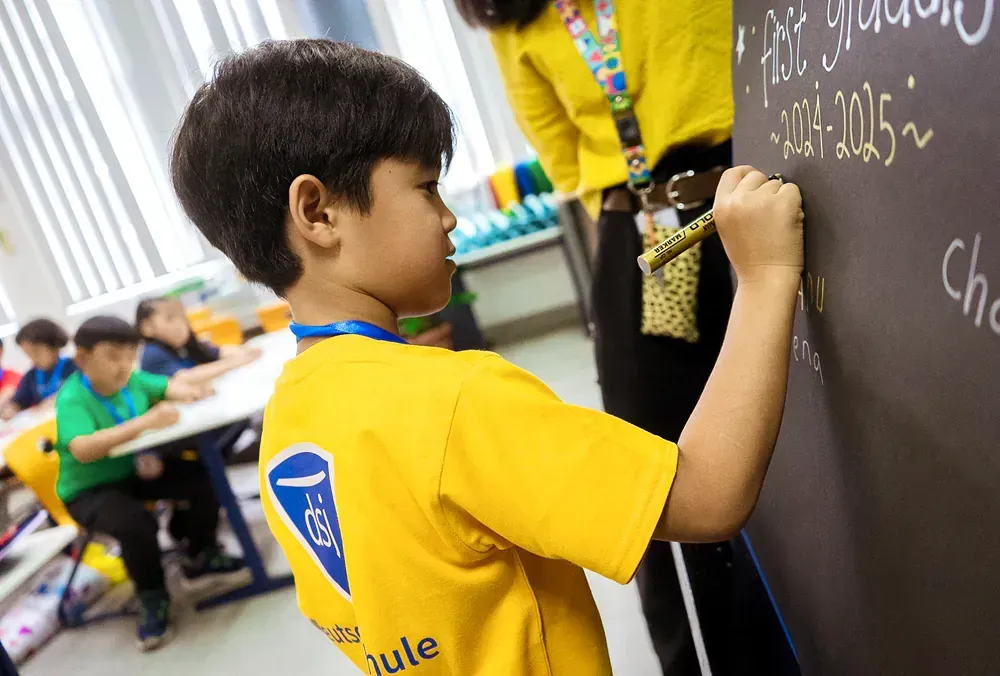 A young boy is writing on a blackboard in a classroom.
