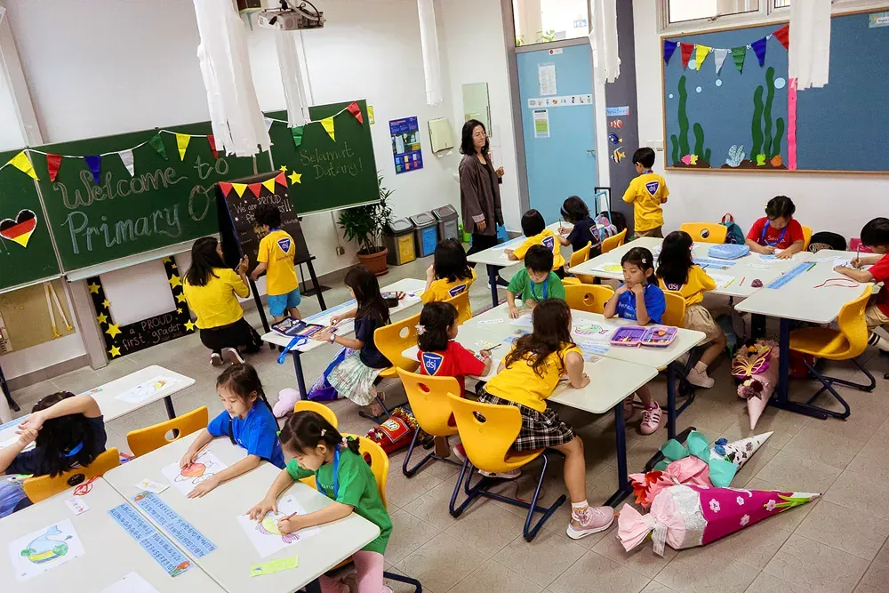 A large group of children are sitting at tables in a classroom.