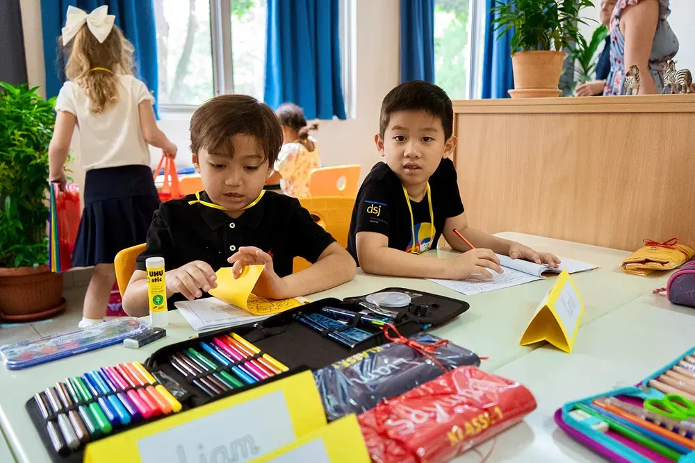 Two young boys are sitting at a table in a classroom.