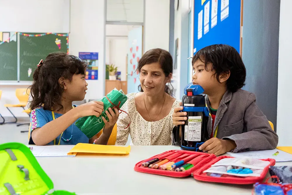 A woman is sitting at a table with two children in a classroom.