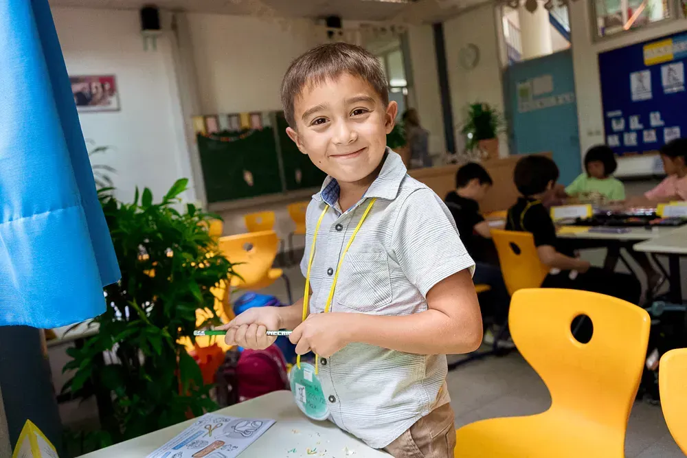 A young boy is sitting at a table in a classroom.