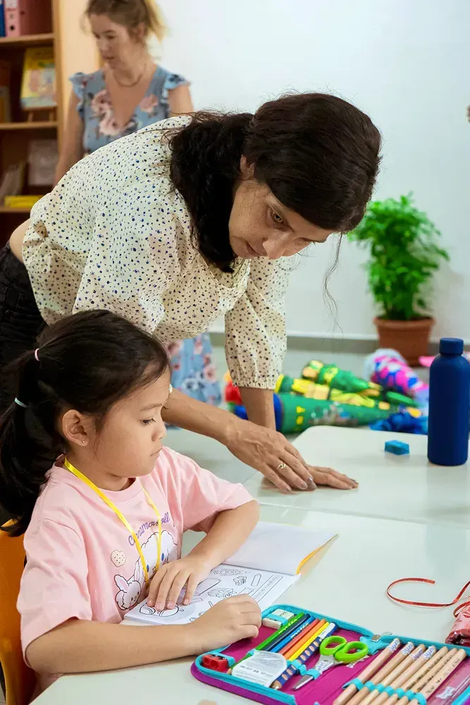 A woman is helping a little girl with her homework in a classroom.