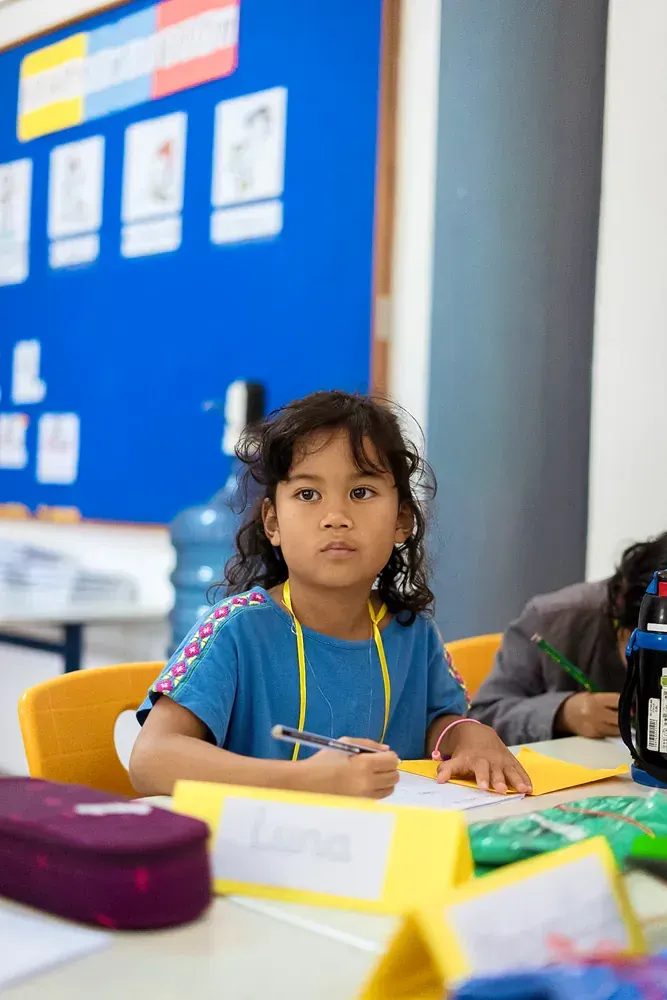 A young girl is sitting at a desk in a classroom.