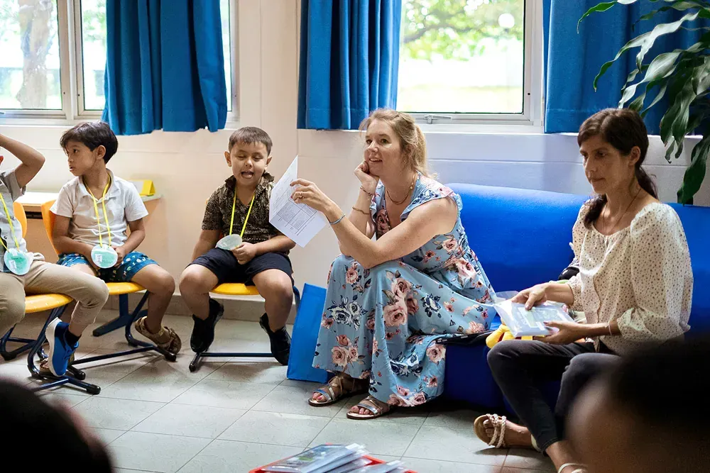 A woman is sitting on a blue couch talking to a group of children.