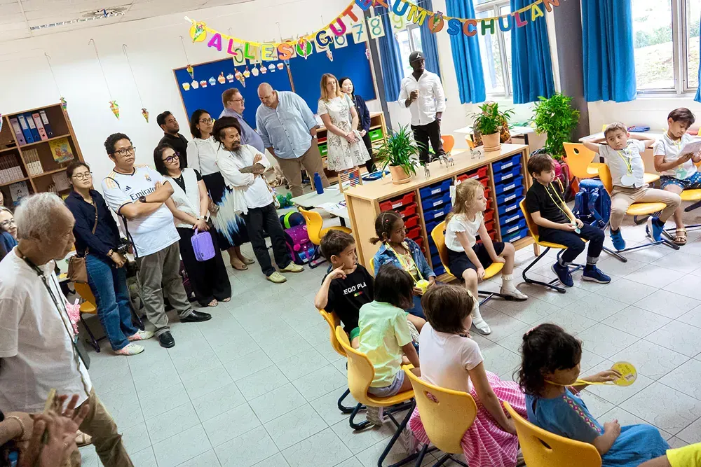 A group of people are standing around a group of children in a classroom.