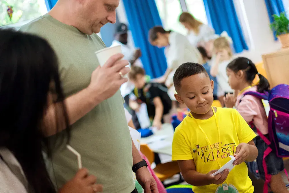 A man is standing next to a boy in a yellow shirt in a classroom.
