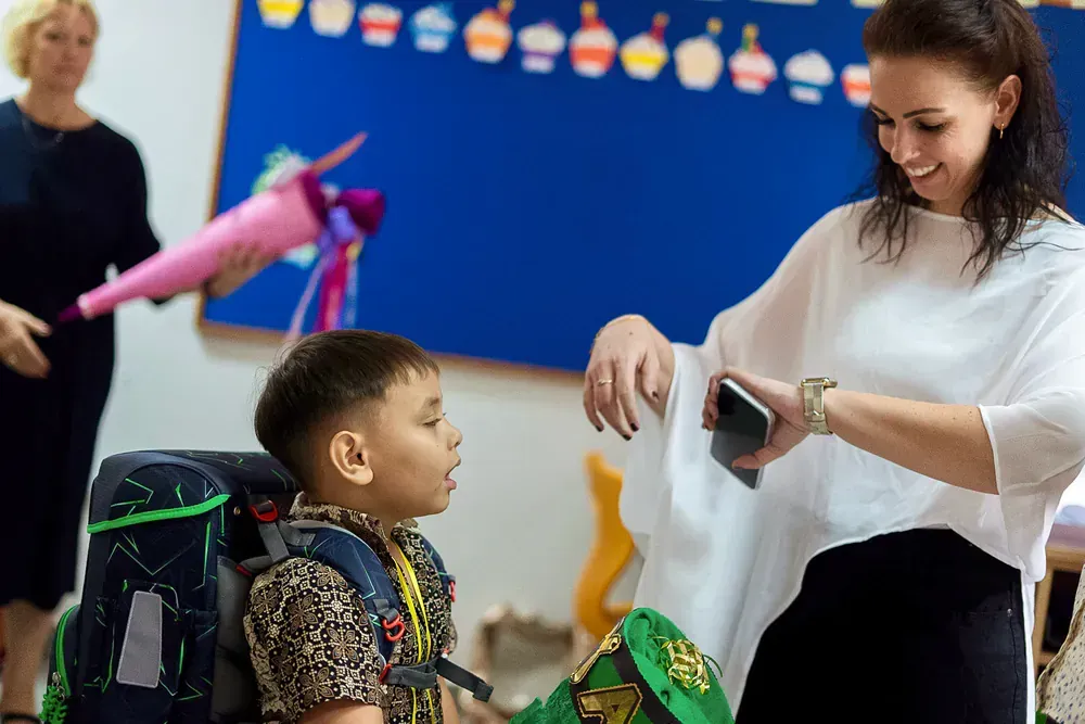 A woman is taking a picture of a young boy in a classroom.